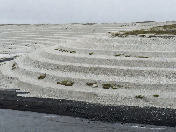 Concentric pale gravel raised beach ridges stepping upward from a dark Arctic shoreline